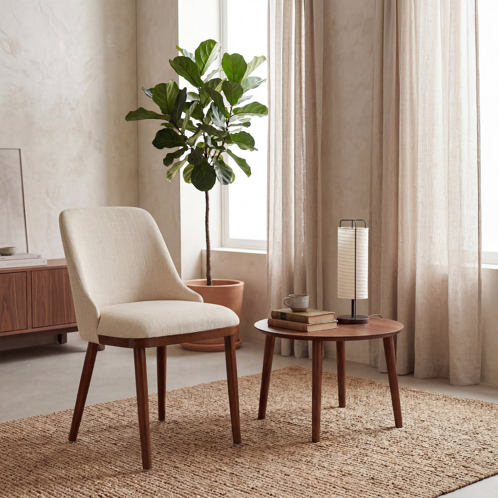 Modern Upholstered Dining Chair in cream fabric beside a round walnut table and fiddle leaf fig