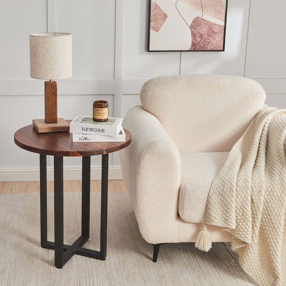 Round End Table in walnut with black X-base beside a cream boucle armchair with a lamp and books